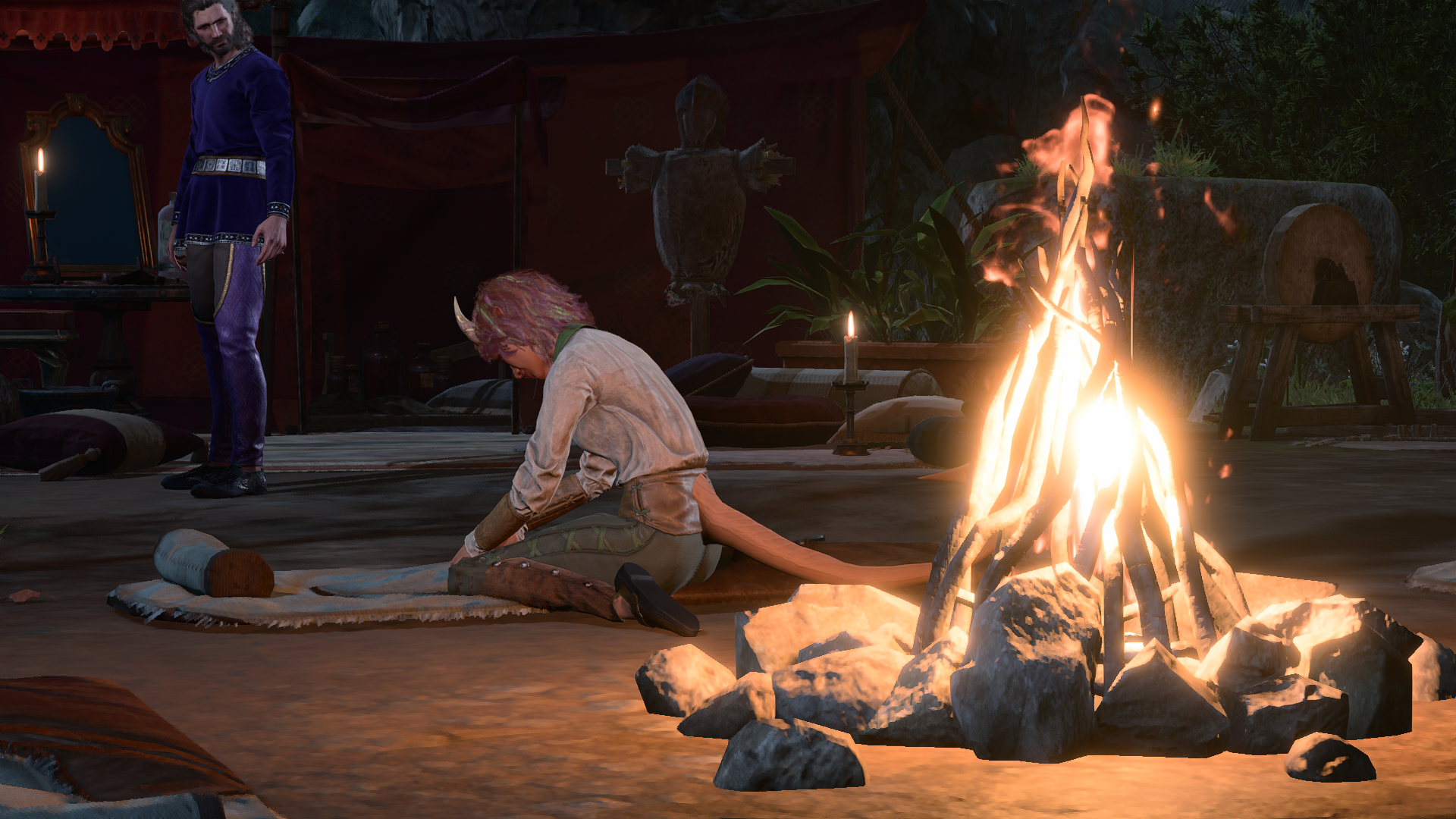 Capture montrant Mel de profil, assise sur sa paillasse à proximité du feu de camp, les jambes en W. Un peu plus loin, Gayle est debout et a le regard nonchalamment tourné vers les mains de Mel qui ne le voit pas, occupée à écrire.